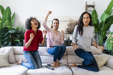 Drei aufgeregte Frauen auf der Couch zu Hause, die fernsehen und jubeln - GIOF05548