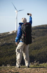 Spanien, Andalusien, Tarifa, Mann auf einem Wanderausflug macht ein Selfie mit Windrad im Hintergrund - KBF00418