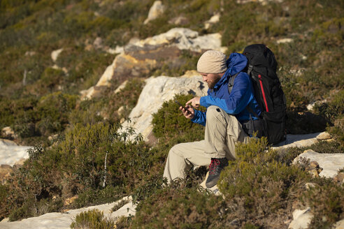 Spain, Andalusia, Tarifa, man on a hiking trip sitting down using cell phone - KBF00421