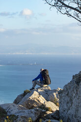 Spanien, Andalusien, Tarifa, Mann beim Wandern an der Küste, auf einem Felsen sitzend und die Aussicht betrachtend - KBF00429