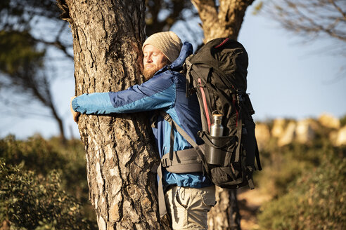 Mann beim Wandern, der einen Baum umarmt - KBF00431