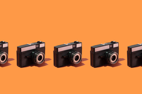 Plastic photo cameras organized in a row over orange background - DRBF00133
