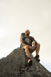 Spanien, Andalusien, Tarifa, lächelnder Mann auf einer Wanderung, der auf einem Felsen sitzend eine Pause macht - KBF00432