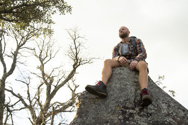 Spanien, Andalusien, Tarifa, lächelnder Mann auf einer Wanderung, der auf einem Felsen sitzend eine Pause macht - KBF00433