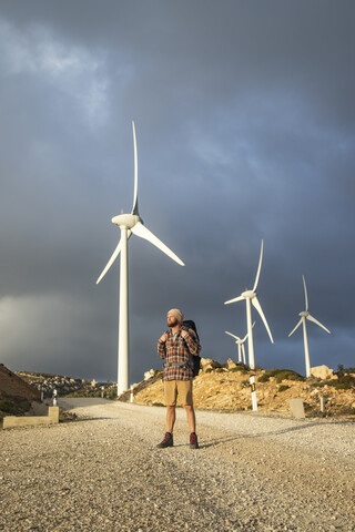 Spanien, Andalusien, Tarifa, Mann beim Wandern auf unbefestigtem Weg mit Windrädern im Hintergrund, lizenzfreies Stockfoto