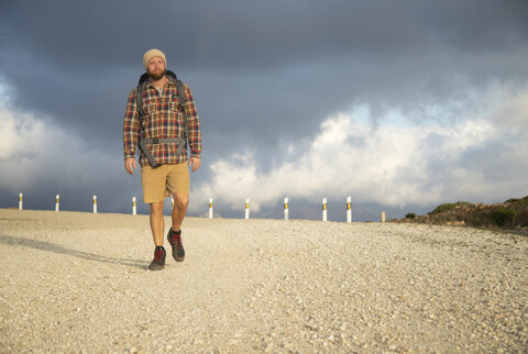 Spanien, Andalusien, Tarifa, Mann auf Wanderschaft auf unbefestigtem Weg unter bewölktem Himmel, lizenzfreies Stockfoto