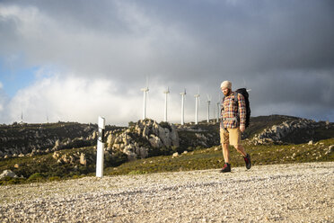 Spanien, Andalusien, Tarifa, Mann auf Wanderschaft auf unbefestigtem Weg mit Windkraftanlagen im Hintergrund - KBF00439