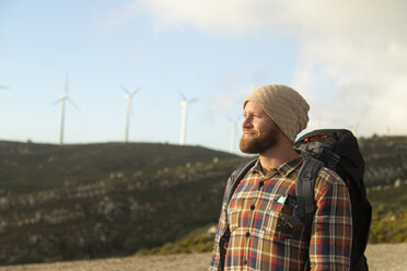 Spanien, Andalusien, Tarifa, lächelnder Mann auf einem Wanderausflug mit Windkraftanlagen im Hintergrund - KBF00441