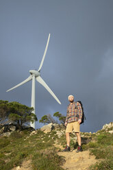 Spain, Andalusia, Tarifa, man on a hiking trip standing on trail with wind turbine in background - KBF00443