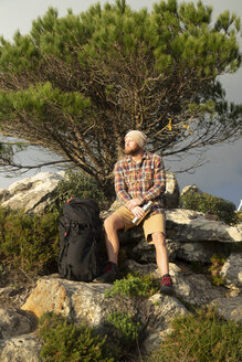 Spanien, Andalusien, Tarifa, Wanderer, der auf einem Felsen sitzend eine Pause macht - KBF00445