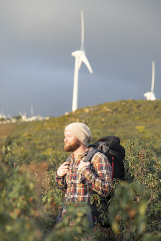 Spanien, Andalusien, Tarifa, lächelnder Mann auf einem Wanderausflug mit Windkraftanlagen im Hintergrund, lizenzfreies Stockfoto