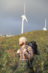 Spain, Andalusia, Tarifa, smiling man on a hiking trip with wind turbines in background - KBF00449