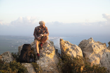 Spanien, Andalusien, Tarifa, Mann auf Wandertour an der Küste auf einem Felsen sitzend - KBF00452