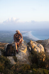 Spain, Andalusia, Tarifa, man on a hiking trip at the coast sitting on rock - KBF00453
