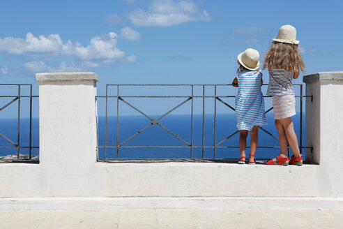 Zwei Mädchen mit Sonnenhüten blicken von einer Mauer auf das Meer hinaus, Erice, Sizilien, Italien - CUF47894