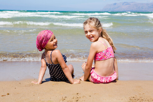 Zwei Mädchen sitzen am Strand und schauen zurück, Porträt, Castellammare del Golfo, Sizilien, Italien - CUF47902