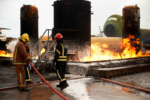 Feuerwehrleute beim Training, Sprühen von Löschschaum auf den Brand eines Öllagertanks in einer Übungsanlage, lizenzfreies Stockfoto