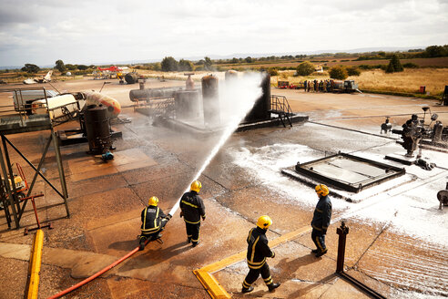 Feuerwehrleute bei der Ausbildung, Feuerwehrleute beim Versprühen von Löschschaum auf einen Öllagertank in einer Ausbildungseinrichtung - CUF47984