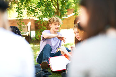 Männliche und weibliche Hochschulstudenten, die auf dem Rasen eines College-Campus über Papierkram diskutieren, Blick über die Schulter - CUF47997