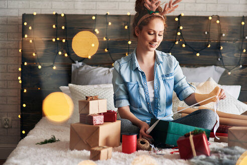 Frau packt Weihnachtsgeschenke auf dem Bett ein - CUF48166