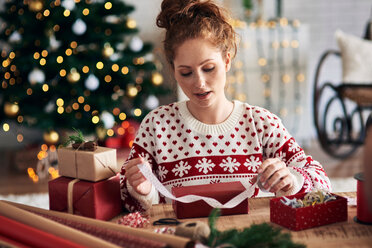 Woman tying ribbon on Christmas present - CUF48168