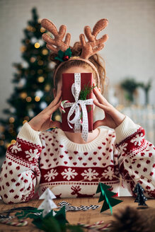 Frau hinter Weihnachtsgeschenk, im Vordergrund weihnachtliche Dekoration in Form eines Weihnachtsbaums - CUF48172