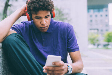 Man texting and using headphones on concrete bench - CUF48194