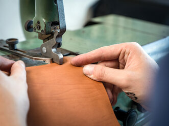 Leatherworker using machining leather handbag edge in workshop, close up of hands - CUF48211