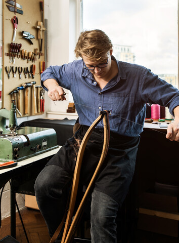 Leatherworker stitching leather handbag straps in workshop stock photo