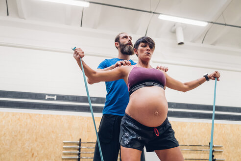 Trainerin führt schwangere Frau mit Seilen im Fitnessstudio an - CUF48216