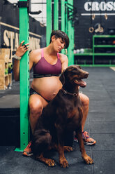 Schwangere Frau und Hund sitzen im Fitnessstudio - CUF48219