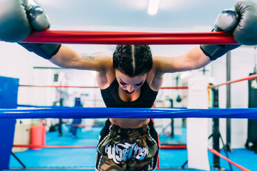 Erschöpfter weiblicher Boxer lehnt sich über die Seile des Boxrings - CUF48241