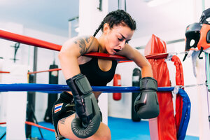 Erschöpfter weiblicher Boxer lehnt sich über die Seile des Boxrings - CUF48244