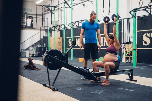 Trainer führt schwangere Frau mit Gewichten im Fitnessstudio an - CUF48254