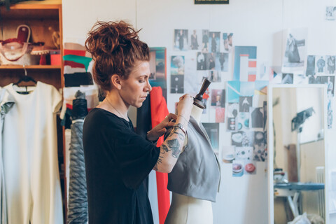 Modedesignerin heftet Kleidungsstück an Schneiderpuppe, lizenzfreies Stockfoto