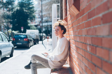 Woman with cellphone on bench on sunny street, Milan, Italy - CUF48276