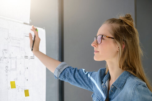 Woman contemplating plans on glass wall - CUF48480