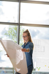 Woman contemplating plans by glass wall - CUF48481