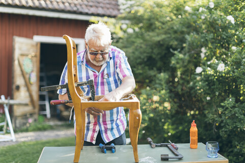 Ein älterer Mann repariert einen Stuhl im Freien in Kvarnstugan, Schweden, lizenzfreies Stockfoto