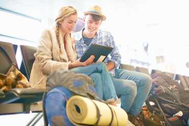 Young couple at airport, sitting, surrounded by backpacks, using digital tablet, low angle view - ISF20122