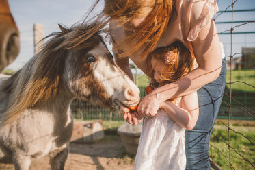 Mother and daughter feeding pony in farm - ISF20141