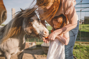 Mutter und Tochter füttern ein Pony auf einem Bauernhof - ISF20141