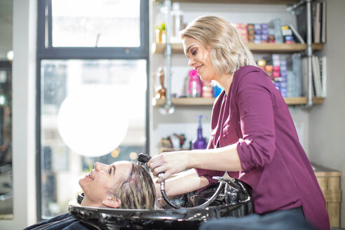 Friseurin spült das Haar eines Kunden im Salon - ISF20144