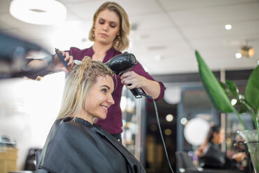Friseurin föhnt das Haar eines Kunden im Salon - ISF20146