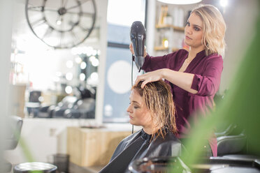 Friseurin föhnt das Haar eines Kunden im Salon - ISF20155