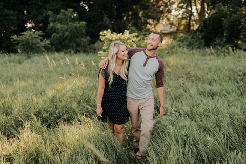 Romantic young woman and boyfriend strolling in field of long grass stock photo
