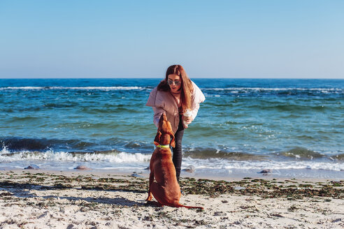 Stilvolle erwachsene Frau am Strand, die ihren Hund streichelt, Odessa, Odeska Oblast, Ukraine - ISF20206