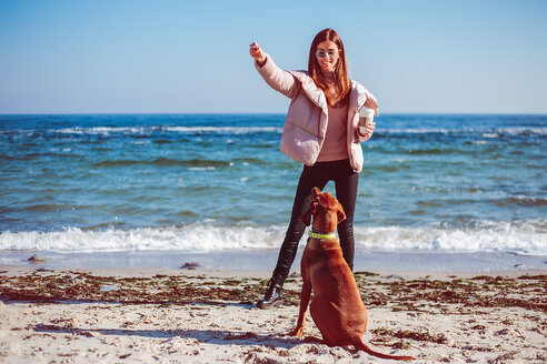 Mittlere erwachsene Frau am Strand, die ihren Hund trainiert, Odessa, Oblast Odeska, Ukraine - ISF20208