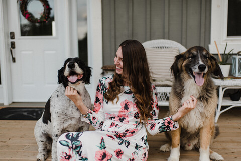 Frau und ihre beiden Hunde sitzen auf der Veranda, lizenzfreies Stockfoto