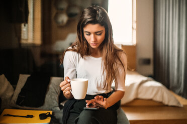 Frau mit Tasse und Smartphone im Schlafzimmer - ISF20260